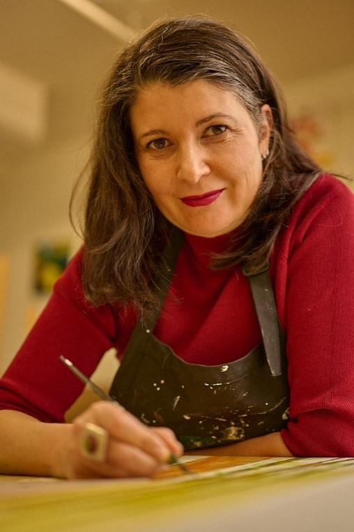 Artist Sandrine Pelissier, in a paint spattered apron, painting in a studio.